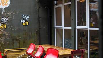 Ulkoterassi, jossa on pöytä ja tuoleja, seinä, jossa on mehiläisteemainen graffitimaalaus, ja rakennus, jossa on ikkunat.