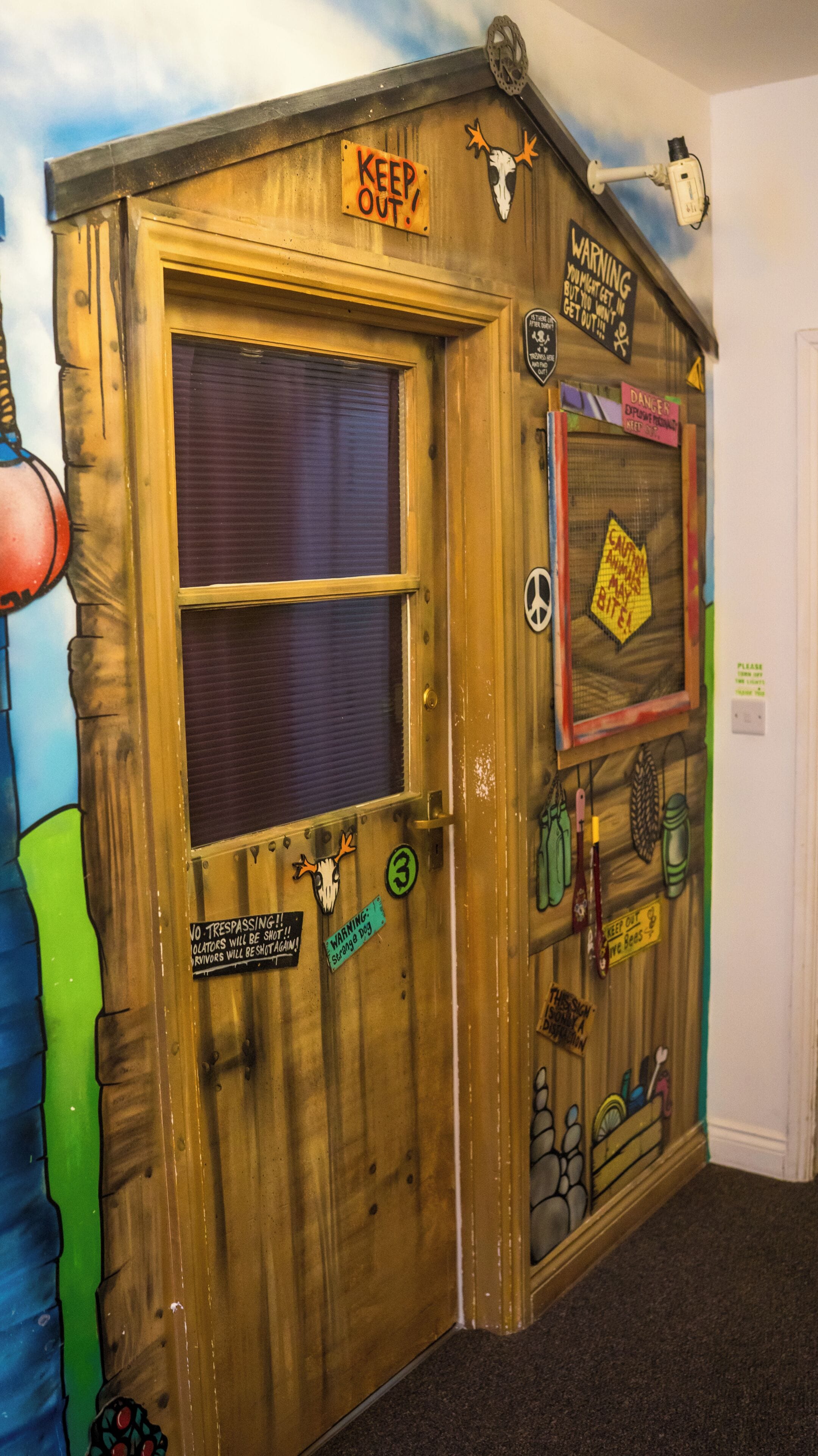 A wooden door with various signs and decorations, including a 'KEEP OUT' sign, a warning sign, and a 'DANGER' sign.