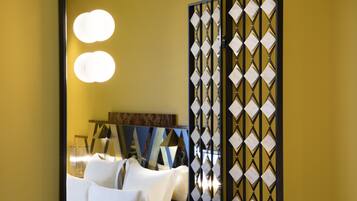 Habitación de hotel con un espejo grande, una cama con ropa de cama blanca y un separador decorativo con un diseño geométrico.