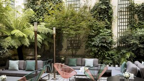 An outdoor seating area with a sofa, chairs, and a table, surrounded by lush greenery and a pergola. - Hotel Saint-Marc (Paris)