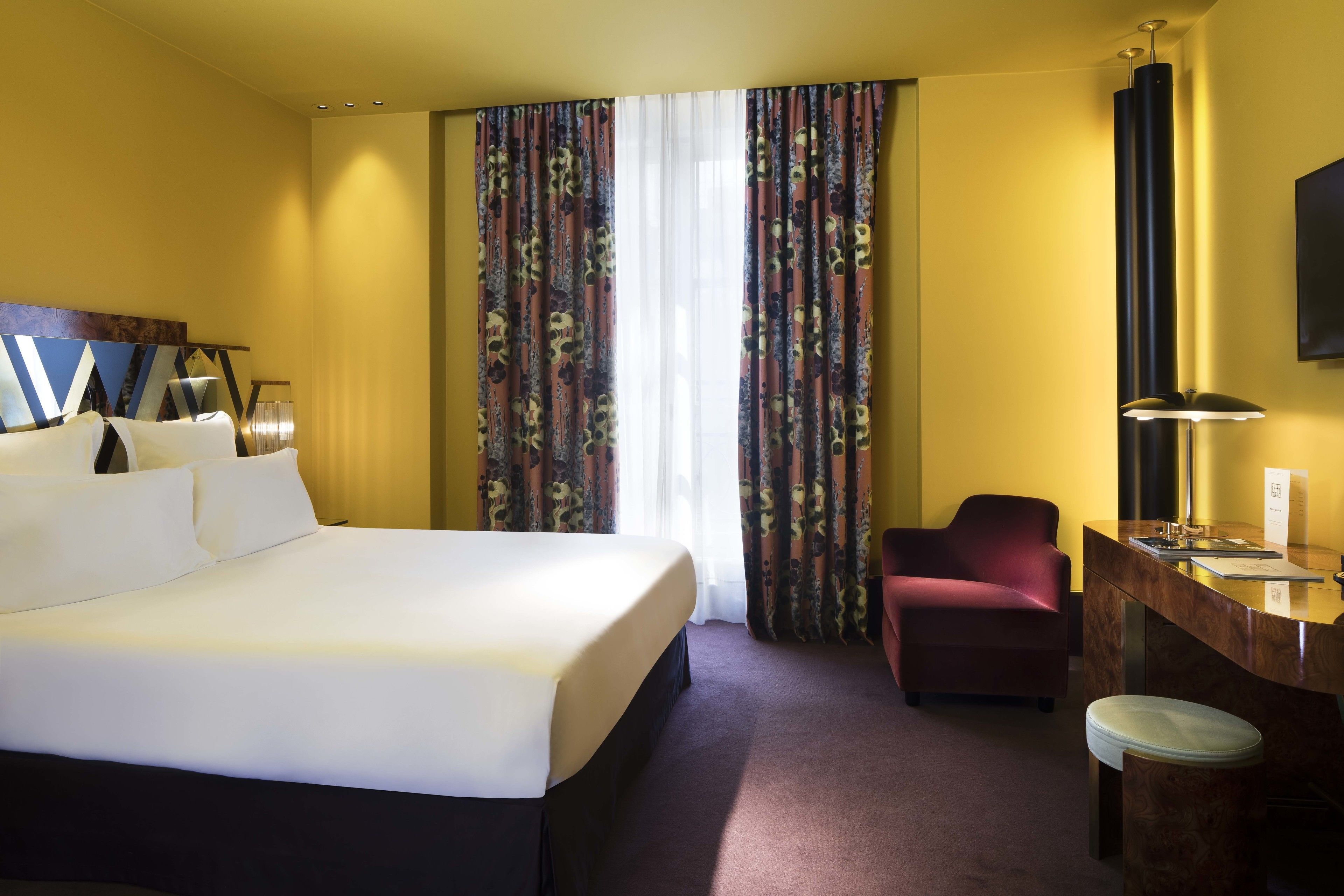 A hotel room with a large bed, a desk, a chair, and a TV.