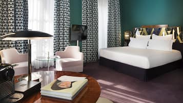 A hotel room with a large bed, a desk with a lamp, a chair, and a TV.