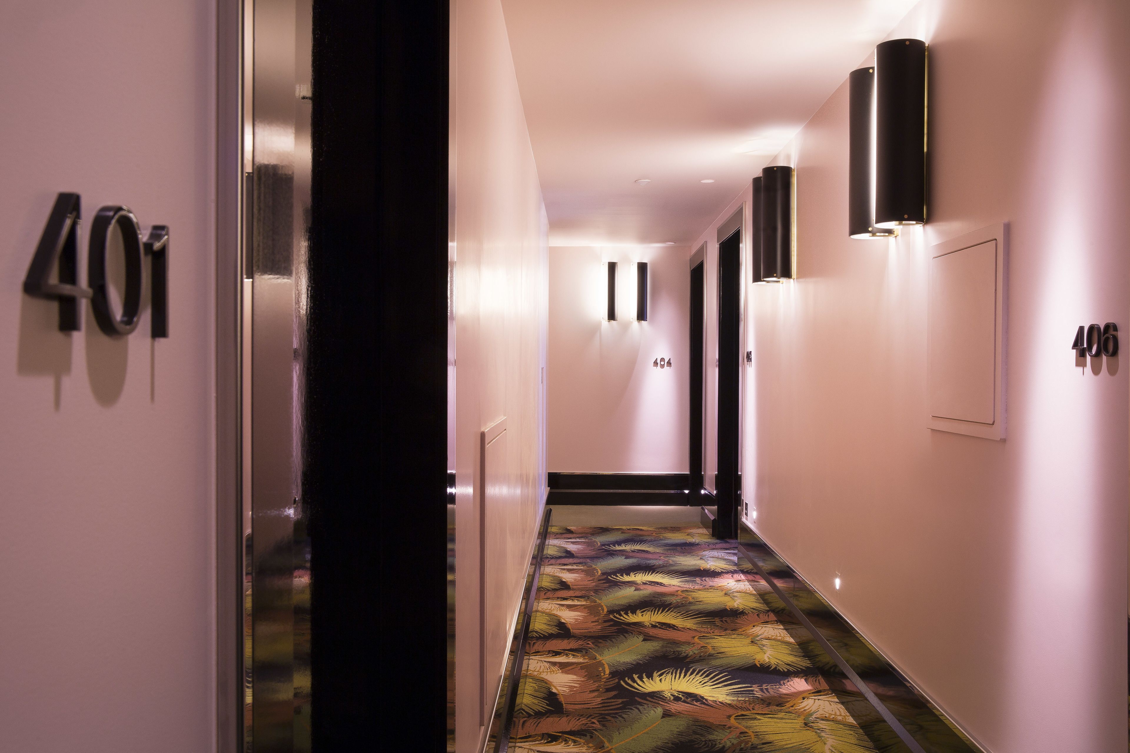 Un pasillo con alfombra estampada, puertas numeradas y luces fijadas a la pared.