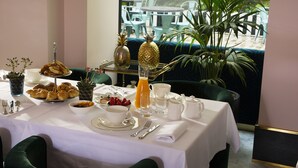 A breakfast table set with croissants, fruit, and beverages, overlooking a garden with chairs and a table. - Hotel Saint-Marc (Paris)