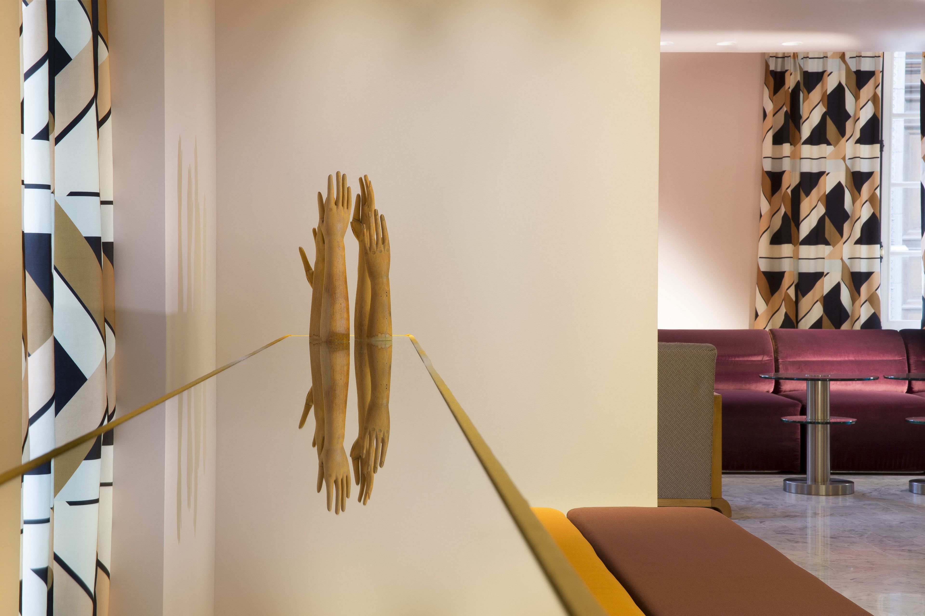 A modern interior with a minimalist design, featuring a wall-mounted sculpture, a patterned curtain, and a seating area with a cushioned bench and a glass table.