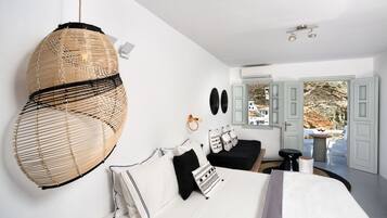 A modern bedroom with a large bed, a hanging rattan chair, a small table, and a view of the outdoors through open doors.