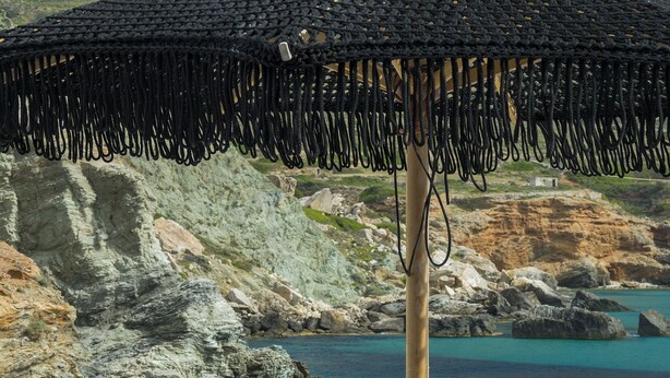 Un área de descanso junto a la playa, con un muro de piedra de fondo, una sombrilla de paja y dos sillas de relax.