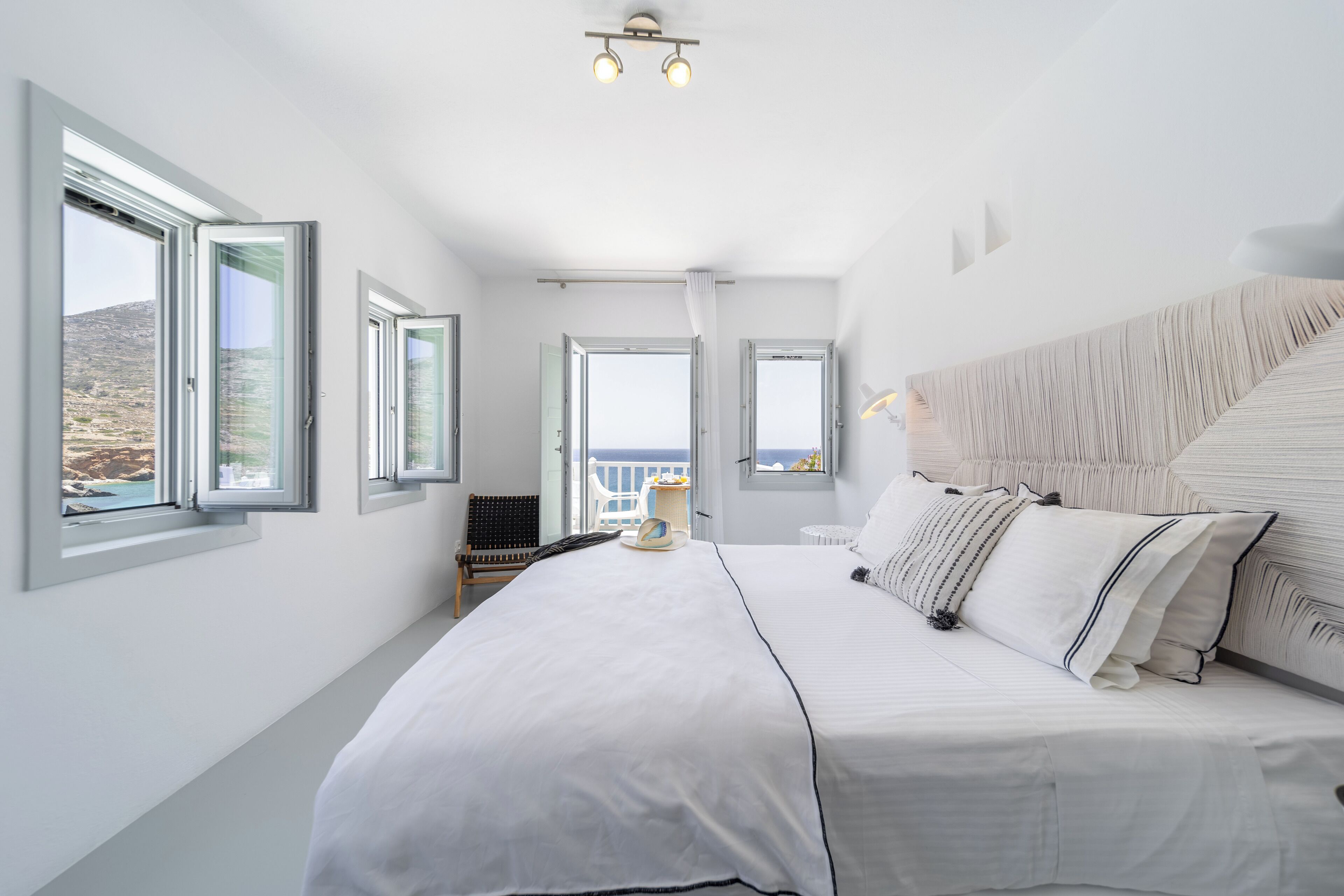 A bedroom with a large bed, multiple windows, a view of the outdoors, and a ceiling light fixture.