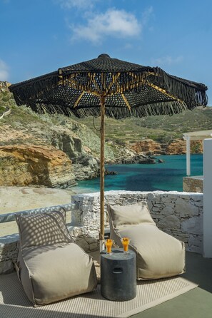 A beachside lounge with a woven umbrella, two cushioned chairs, and a small table with a drink. - Blue Sand Boutique Hotel & Suites (Folegandros)