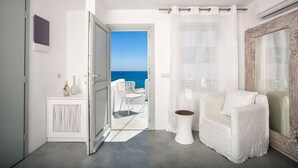 Habitación moderna con una silla blanca, una mesita y vista al mar por una puerta abierta.