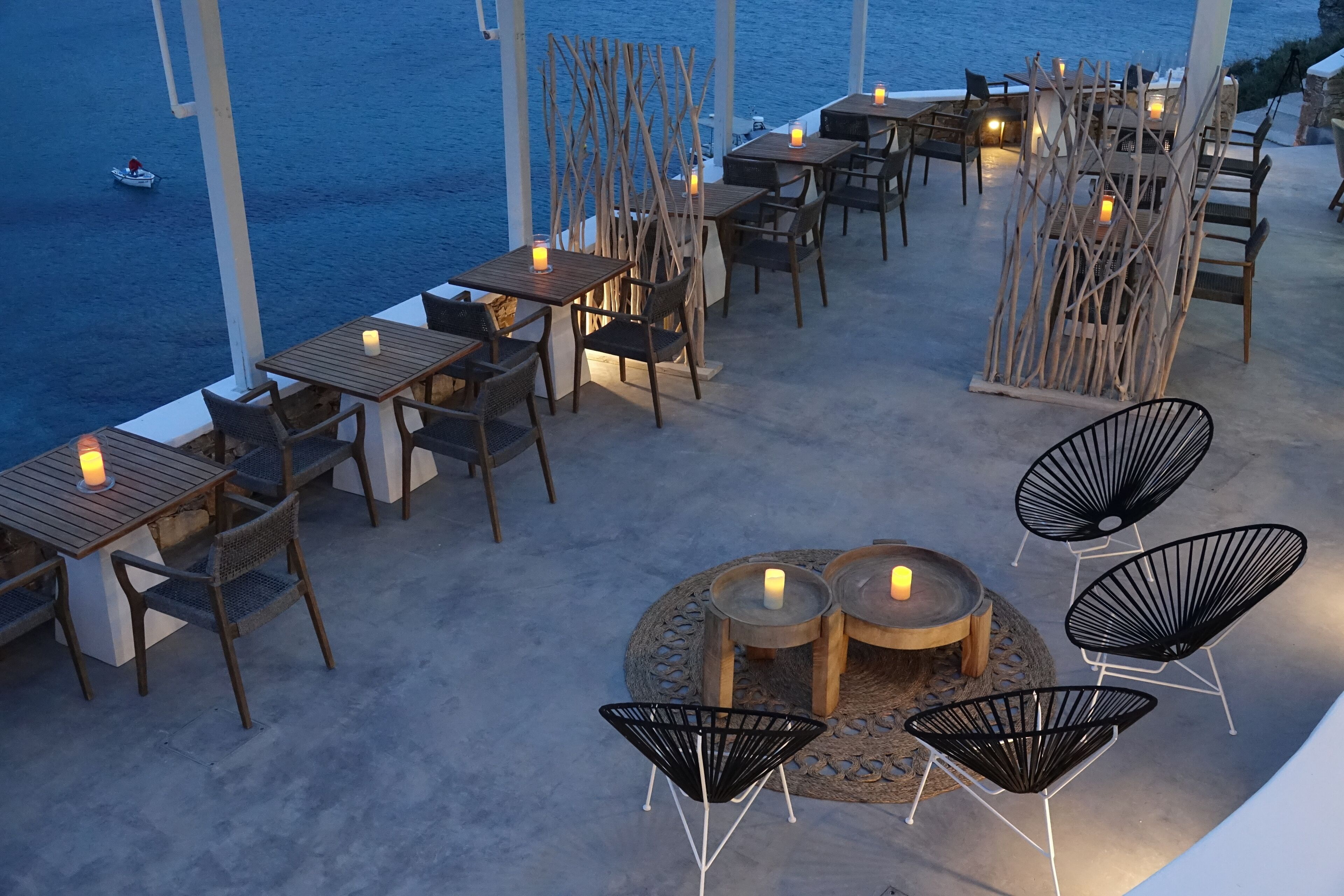Un espace de restauration en plein air avec des tables et des chaises, une table ronde décorée de bougies et une vue sur la mer.