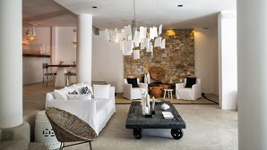 Una sala de estar moderna con pared de piedra, muebles blancos y una lámpara colgante.