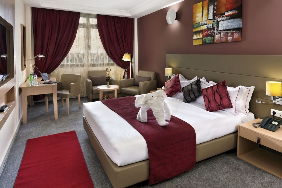 Une chambre d’hôtel avec un grand lit, un bureau, une chaise, une petite table et une table de chevet.