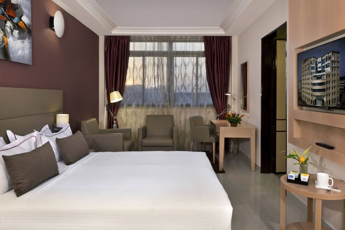 Une chambre d’hôtel avec un grand lit, un bureau, deux chaises, une petite table avec une plante et un tableau au mur.