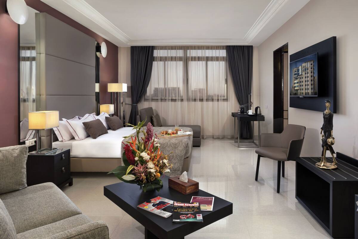 Une chambre d’hôtel moderne comprenant un lit, un coin salon avec une table basse, une télévision et une statue décorative.