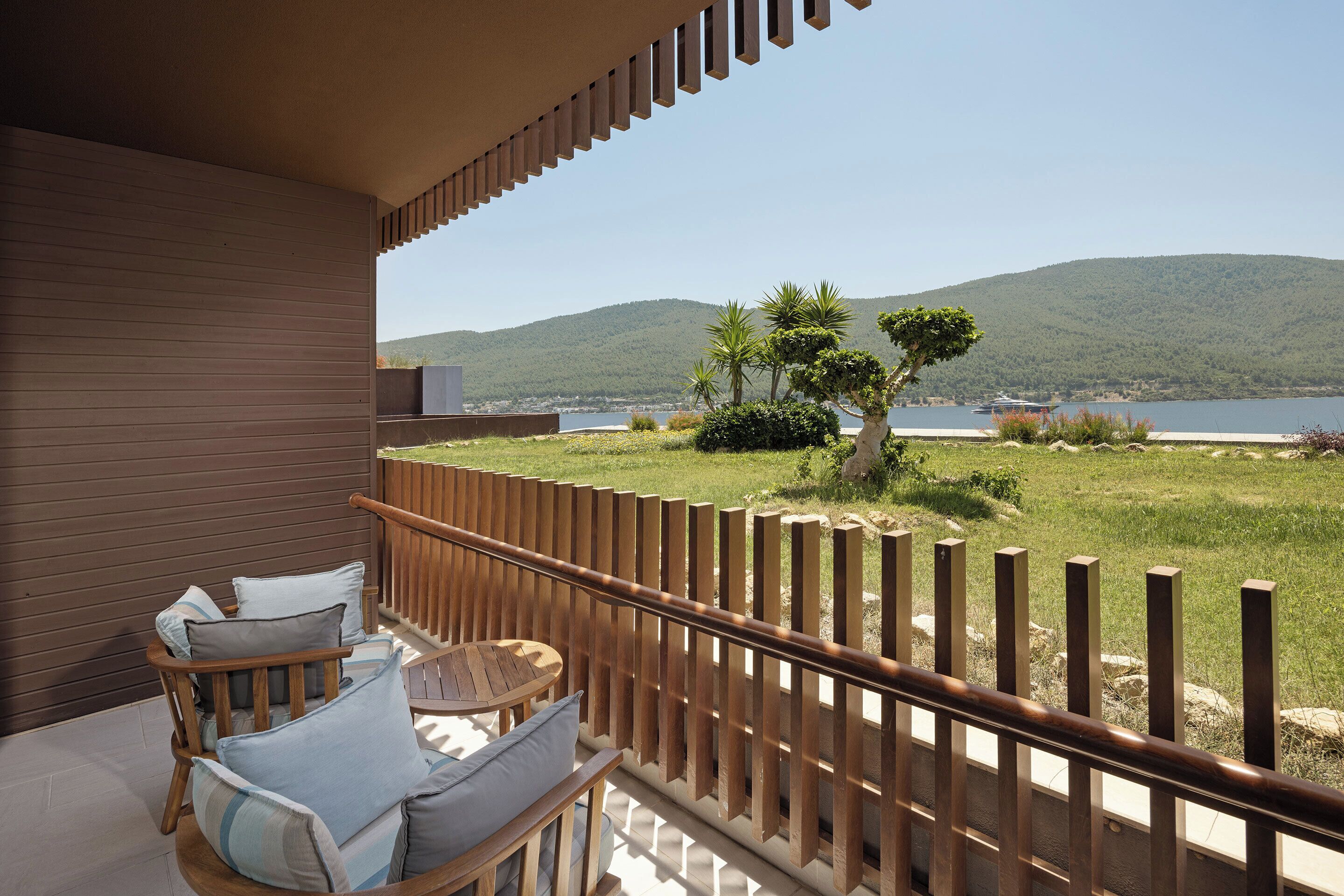 A balcony with wooden railings, a seating area with cushions, and a view of a lake and mountains.