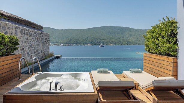 A wooden deck with a hot tub, lounge chairs, and a view of a body of water and mountains. - Titanic Luxury Collection Bodrum - All inclusive (Milas)