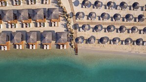 An aerial view of a beach resort with rows of sun loungers and umbrellas, a sandy beach, and clear turquoise water. - Titanic Luxury Collection Bodrum - All inclusive (Milas)