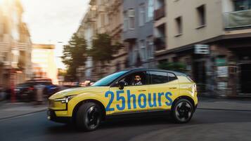 A yellow car with "25 hours" on its side driving on a city street.