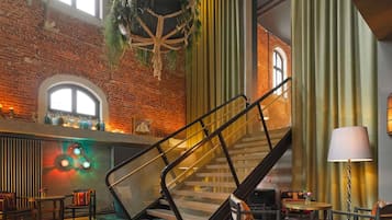 Un vestíbulo de hotel con pared de ladrillo, una escalera, una planta colgante y una mesa con sillas.