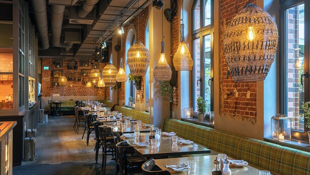 Un restaurant avec de longues tables, des lampes suspendues, des murs en briques et de grandes fenêtres.