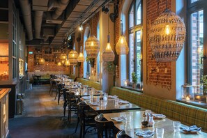A restaurant with long tables, hanging lamps, brick walls, and large windows. - 25hours Hotel Altes Hafenamt (Hamburg)