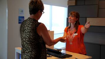 Two individuals at a reception desk with a telephone and a name tag visible.