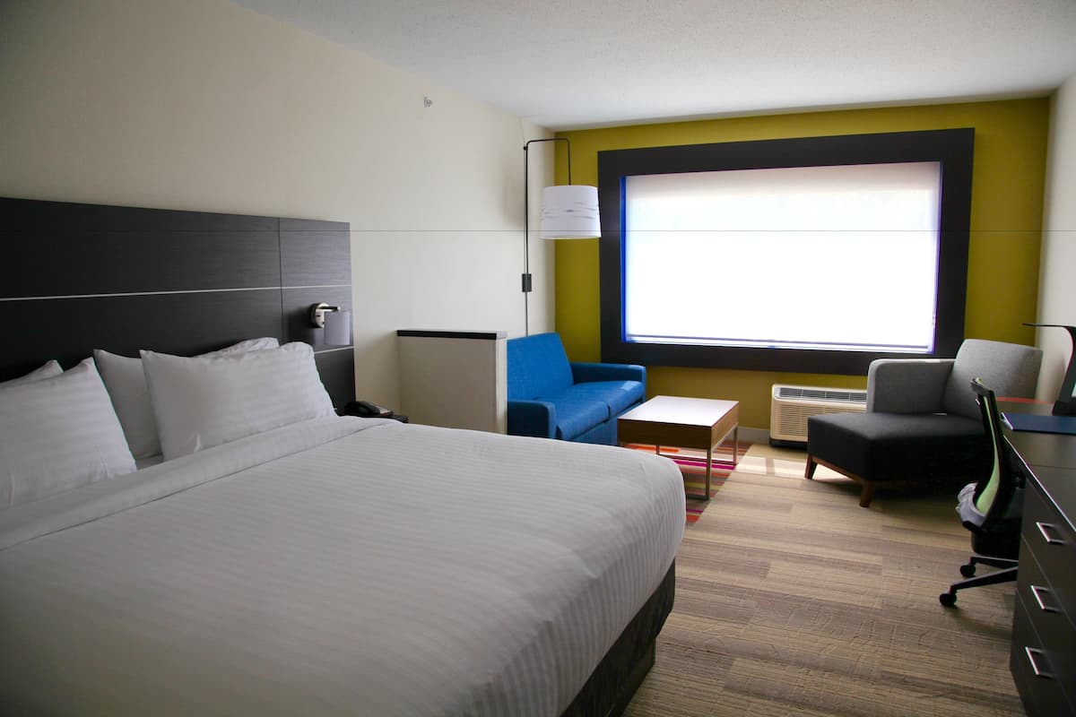 A hotel room with a large bed, a blue sofa, a small table, and a desk with a chair.