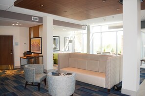 Ett entréområde med en sittgrupp bestående av en soffa och två fåtöljer, en receptionsdisk och en dörr med skylten ”FÖRVARING”.