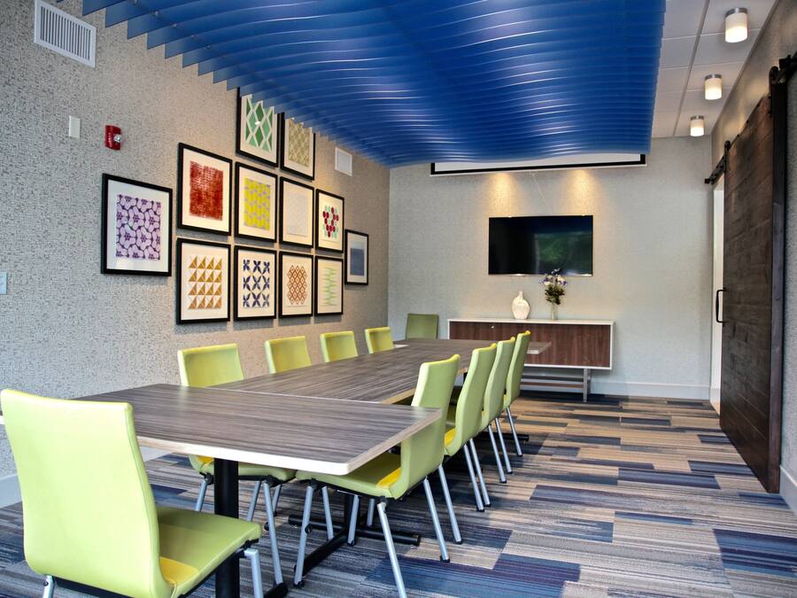 A conference room with a long table, multiple chairs, framed artwork on the wall, a flat-screen TV, and a wooden cabinet.