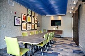 Une salle de conférence avec une longue table, de nombreuses chaises, des œuvres d’art encadrées au mur, un téléviseur à écran plat et un buffet en bois.