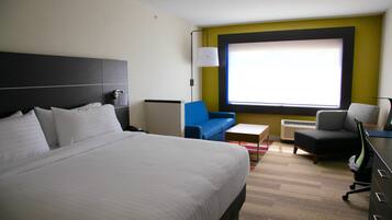 A hotel room with a large bed, a blue armchair, a small table, and a desk with a chair.