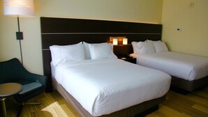 Une chambre d’hôtel avec deux lits, une table de chevet avec une lampe, une petite table et une chaise.