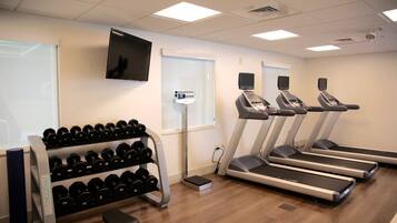 Ett gym med löpband, en ställning för hantlar och en tv på väggen.