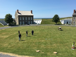 A grassy field with a building in the background, a white fence, and a cart. - Holiday Inn Express & Suites Oswego by IHG (Oswego)