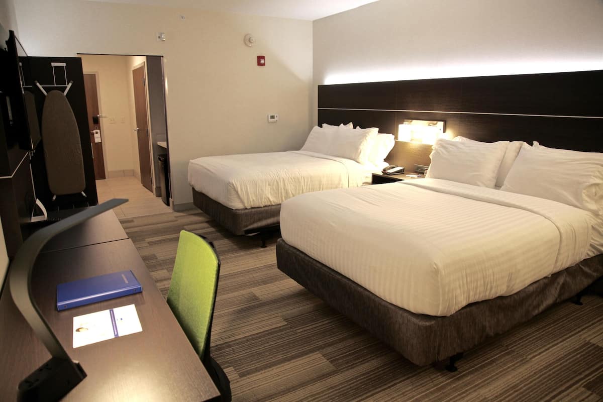 A hotel room with two beds, a desk, a chair, and a small table.