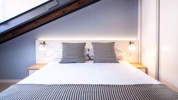 A neatly made bed with a patterned bedspread, two matching pillows, bedside lamps, and a wooden beam above the bed. - Apartment in Malasaña   (Madrid)