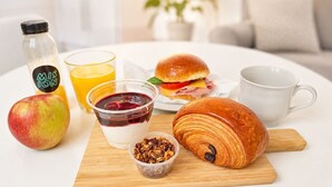 A breakfast setting with a croissant, apple, juice, yogurt, and a sandwich on a wooden board. - Apartment in Malasaña   (Madrid)