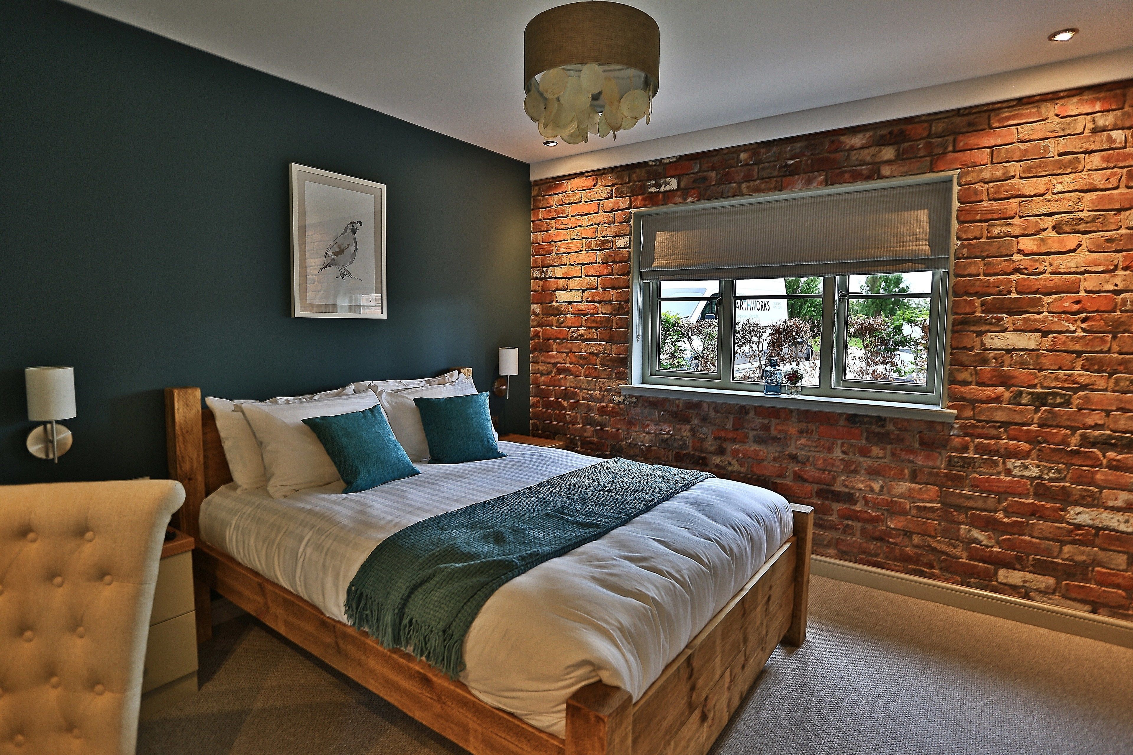 A bedroom with a wooden bed, dark walls, a brick accent wall, and a window with a view.