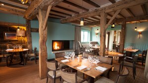 Een restaurant met houten balken, een open haard en gedekte tafels.