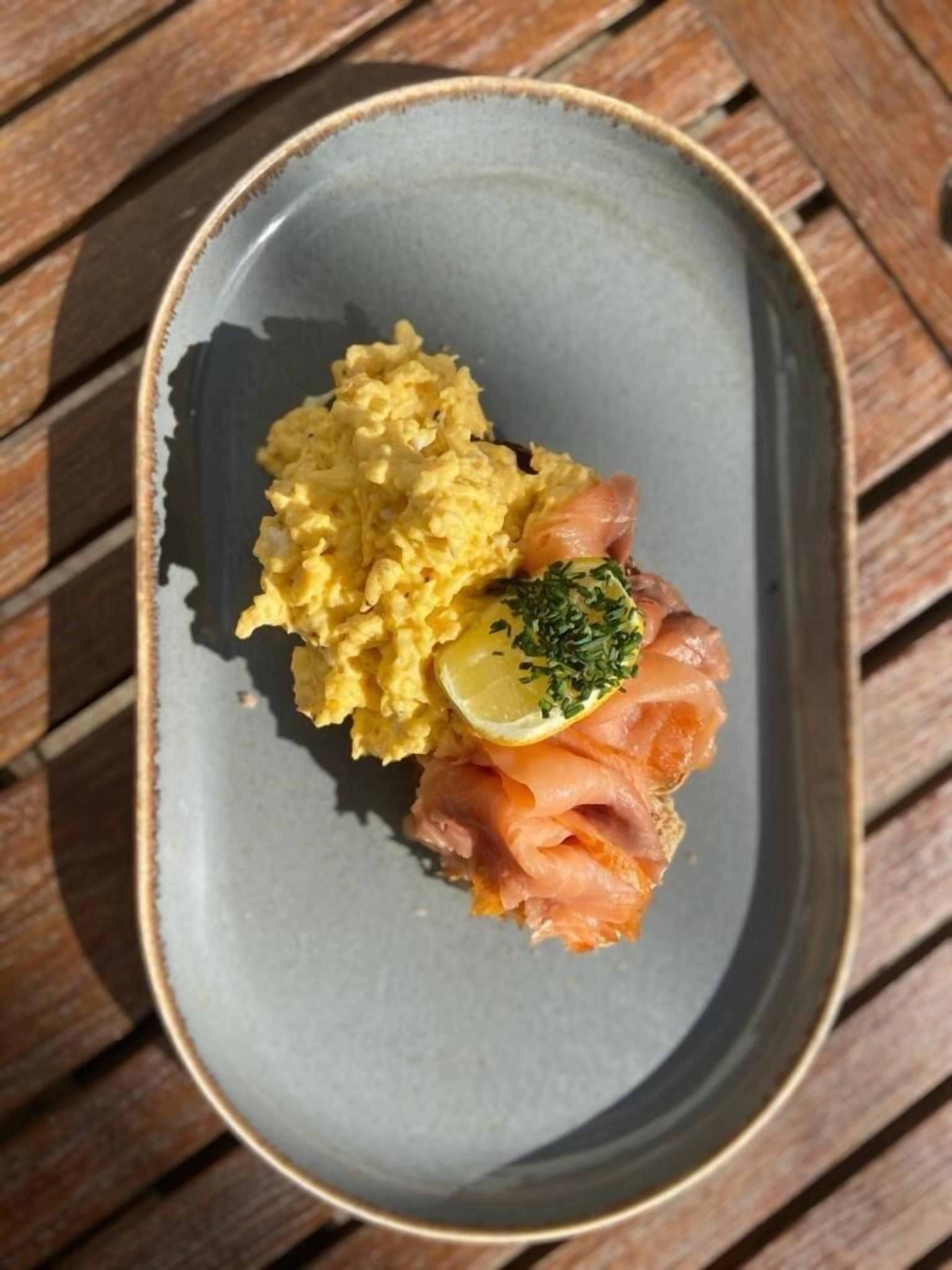 A plate with scrambled eggs, smoked salmon, and a lemon slice on a wooden table.