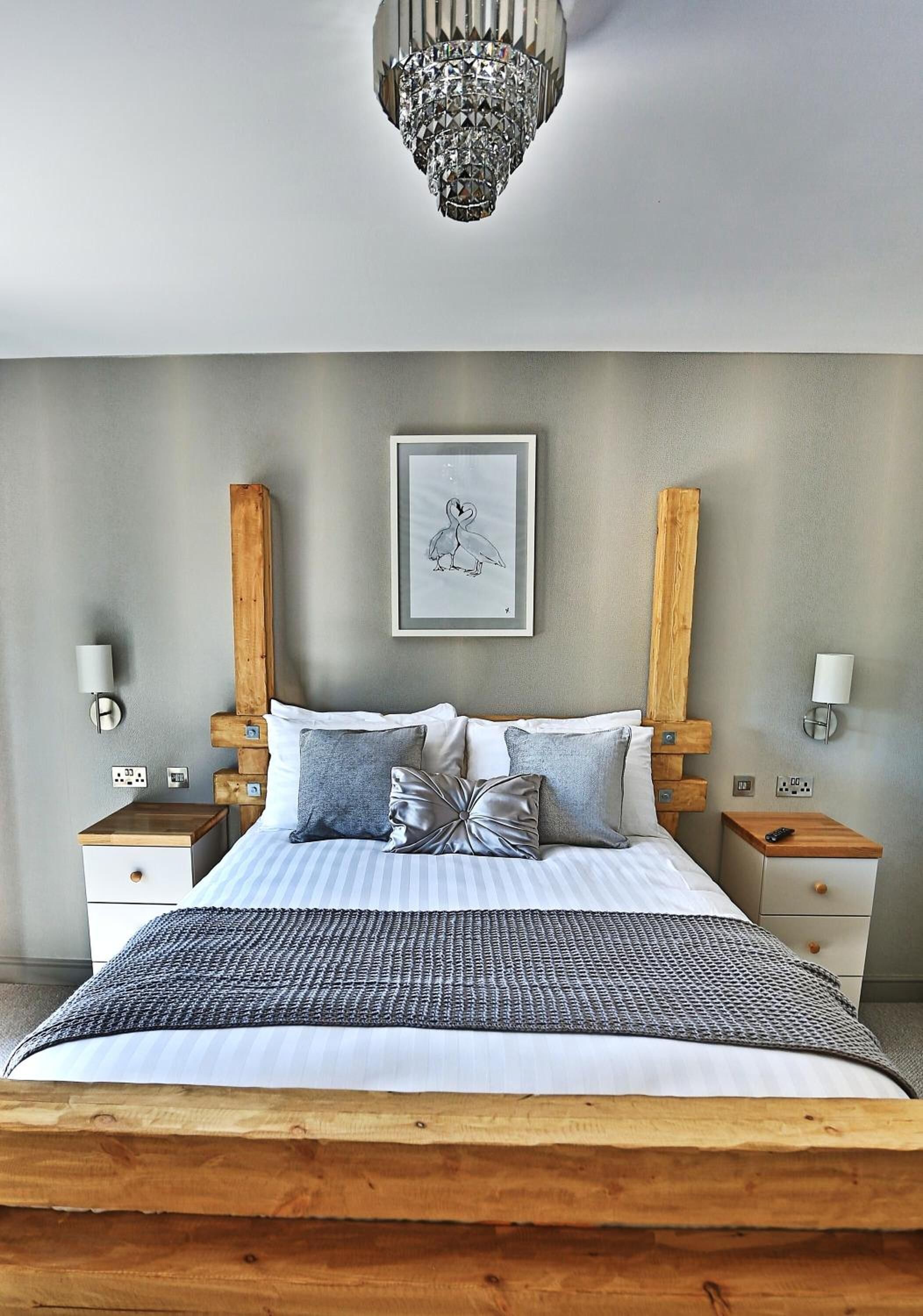 Een slaapkamer met een groot bed, een houten hoofdbord, nachtkastjes, een kroonluchter en een ingelijst kunstwerk aan de muur.