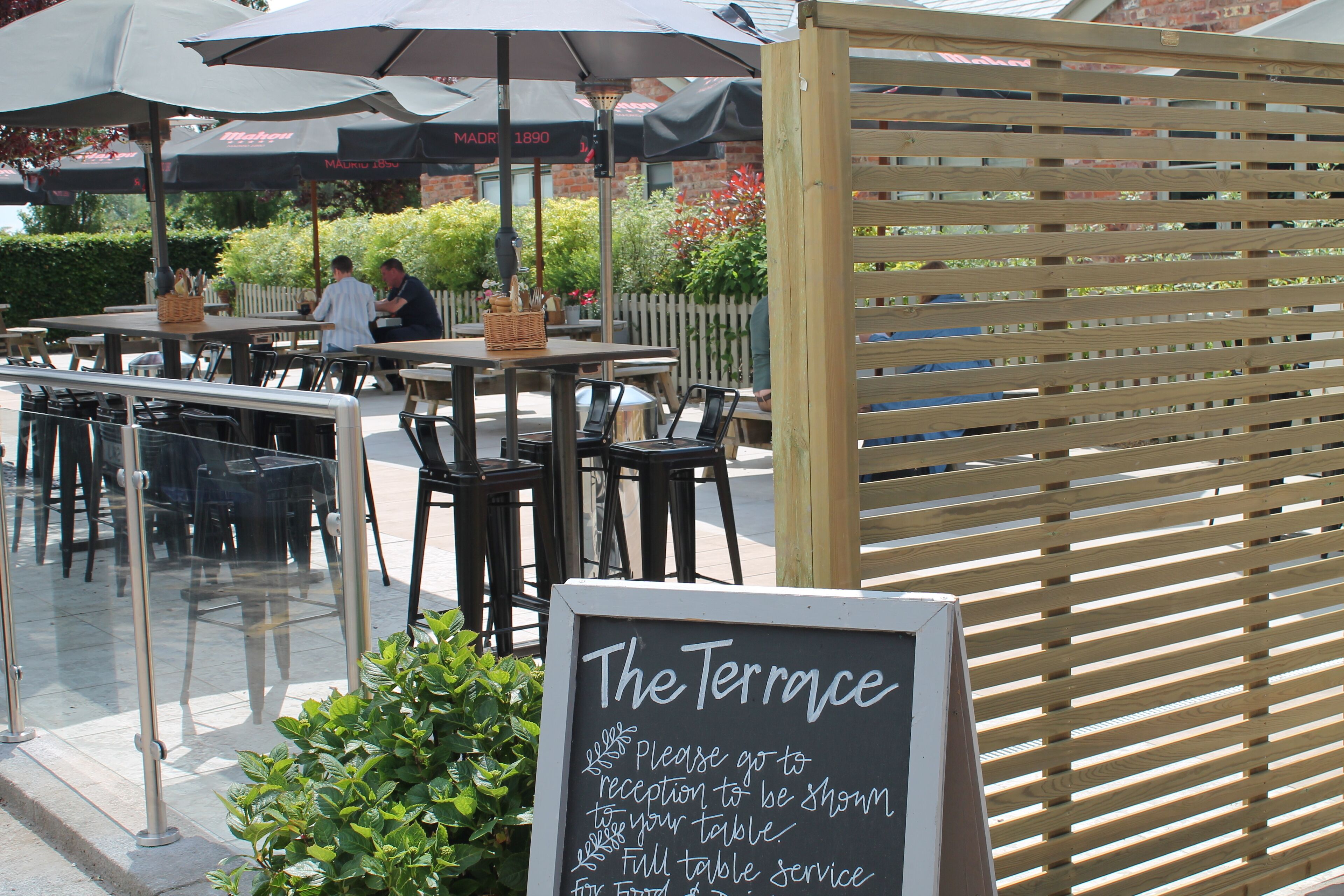 An outdoor dining area with tables and chairs, a wooden fence, and a sign indicating table service.