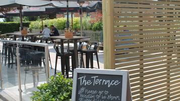 An outdoor dining area with tables and chairs, a wooden fence, and a sign indicating table service.