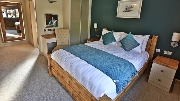 Een slaapkamer met een houten bed, een nachtkastje, een spiegel en een aan de muur hangend schilderij.