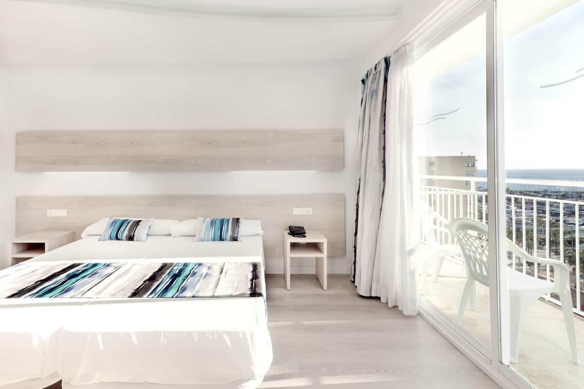 Une chambre d’hôtel moderne avec un grand lit, un petit bureau et un balcon offrant une vue sur la ville.