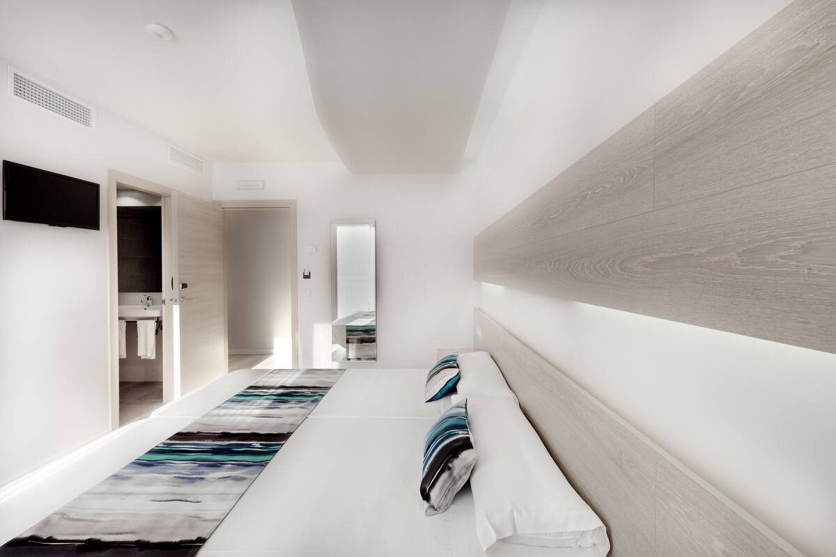Une chambre d’hôtel moderne, de forme longue et étroite, dotée d’un grand miroir, d’un téléviseur à écran plat et d’un mur décoratif en bois.