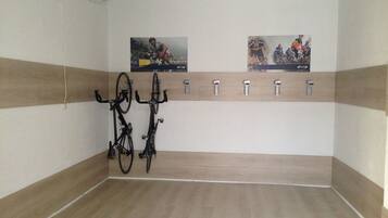 Una habitació amb un terra de fusta, dues bicicletes penjades a la paret i dos cartells.