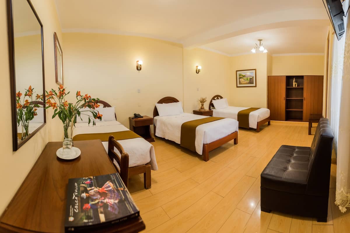 Habitación de hotel con dos camas, un sofá, una mesa de comedor y un televisor.