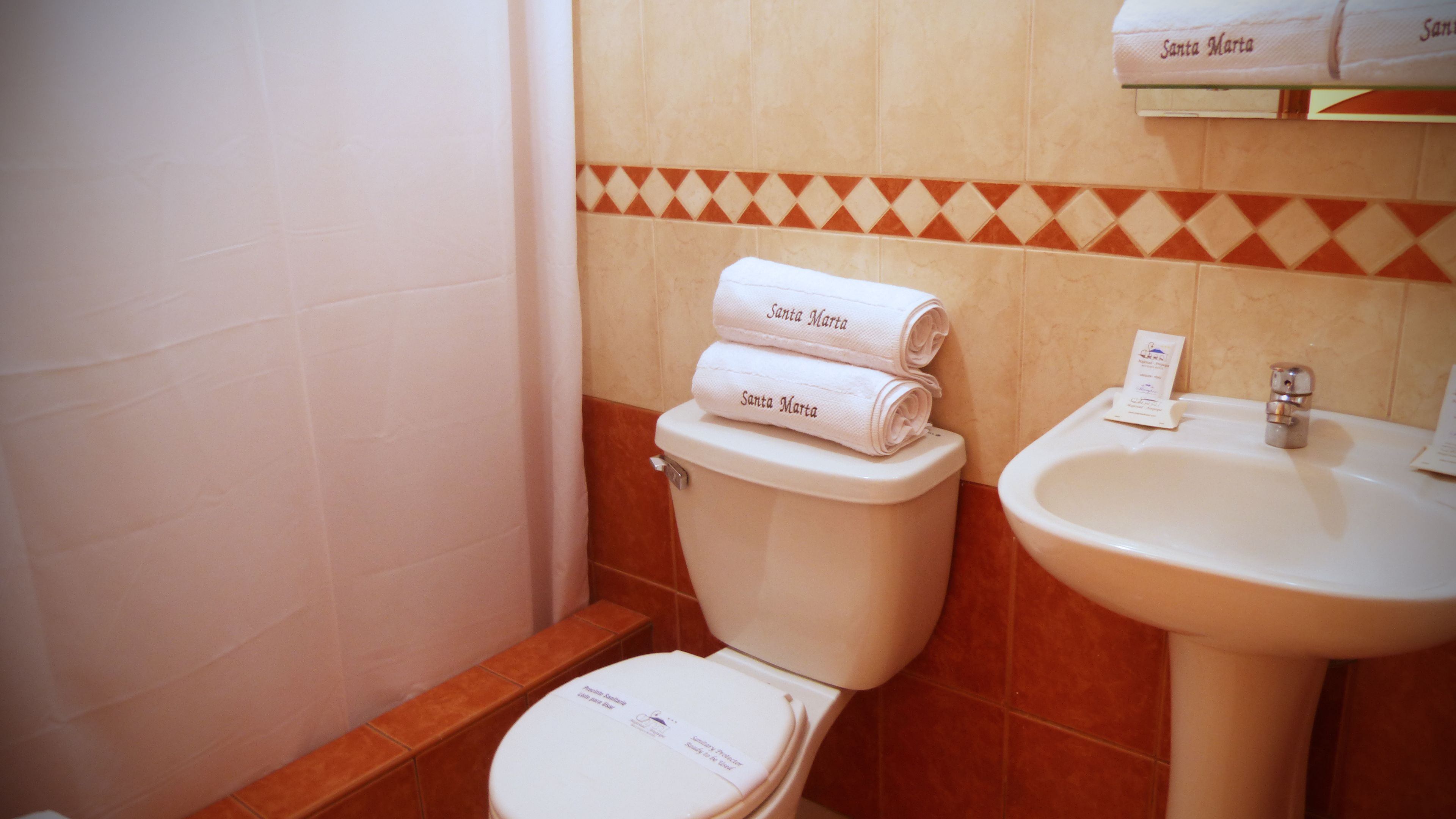 A bathroom with a toilet, a sink, and two rolled towels labeled 'Santa Marta'.